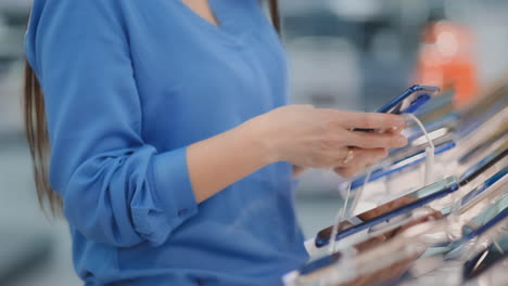 Close-up-woman-in-an-electronics-store-holding-a-new-smartphone-picks-before-buying-on-the-showcase