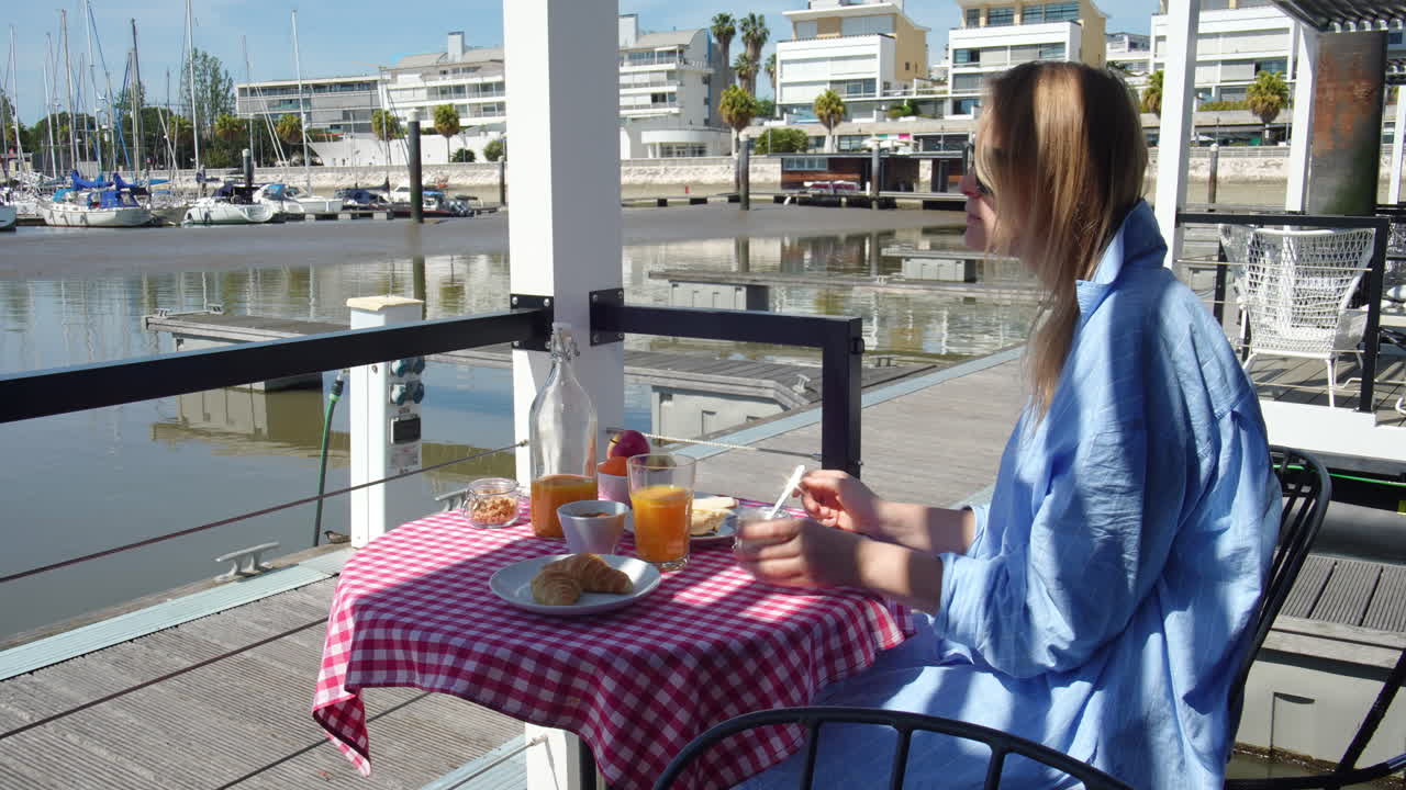 Woman having breakfast on a terrace overlooking a marina