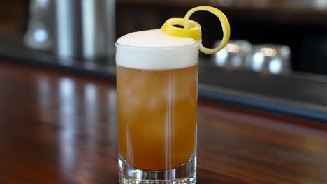 a cocktail with a foamy top and lemon peel garnish on a bar counter