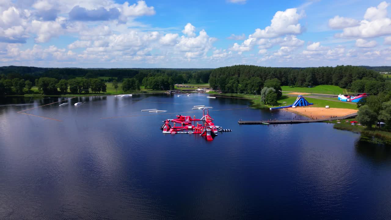 Wide panoramic aerial shot of Zarasai lake, inflatable park, and lush landscape extending toward the horizon. Shot in Zarasai, Lithuania (Zarasai, Lietuva)