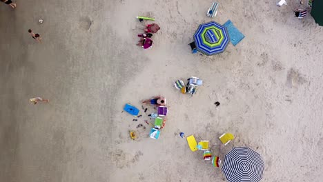 Toma-Aérea-De-Arriba-Hacia-Abajo-De-Familias-Y-Parejas-Relajándose-En-Una-Playa-De-Arena