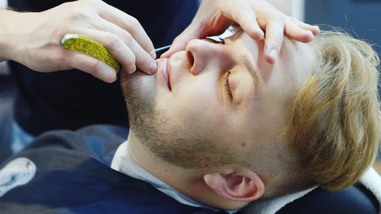 un joven se afeita con una maquinilla de afeitar peligrosa en un video hd de barbería