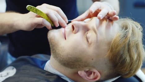 un joven se afeita con una maquinilla de afeitar peligrosa en un video hd de barbería