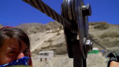 close detail shot as a woman crossing a river with a rope swing metal wheel suspension rolling.
