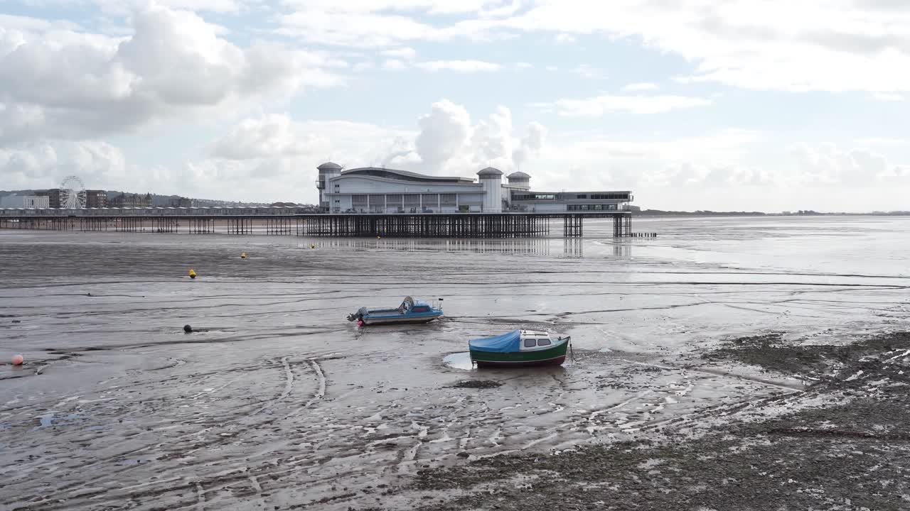 última sección del gran muelle weston-super-mare con un cielo nublado y azul en el fondo, pequeños barcos de pesca amarrados en los bancos de arena