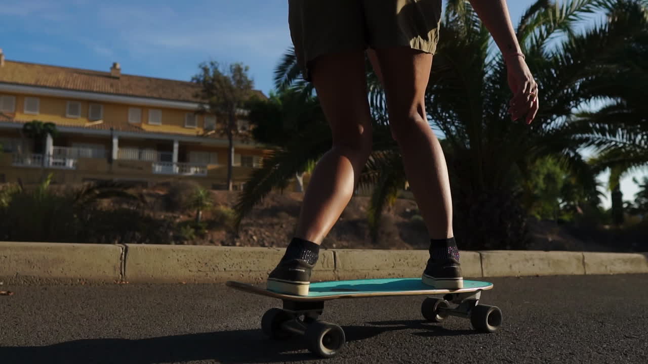 con palmeras como telón de fondo, una mujer joven navega en un longboard en cámara lenta, vestida con pantalones cortos y zapatillas de deporte durante el verano