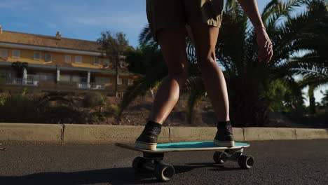 with palm trees as backdrop, a young woman cruises on a longboard in slow motion, dressed in shorts and sneakers during summer