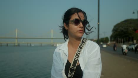 young indian woman putting on her sunglasses next to a promenade and a river