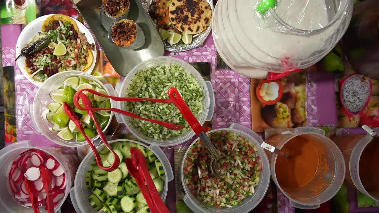 Top-down view of a Mexican street food table with tacos, burritos, and bowls of fresh ingredients such as salsa, spices, cucumber, radish, and salad, capturing variety, flavor, and street food culture
