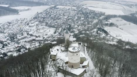 Drone-aerial-of-the-fairy-tale-castle-Plesse-in-winter-with-a-huge-amount-of-snow-on-a-beautiful-mountain-near-Bovenden,-Germany,-Europe