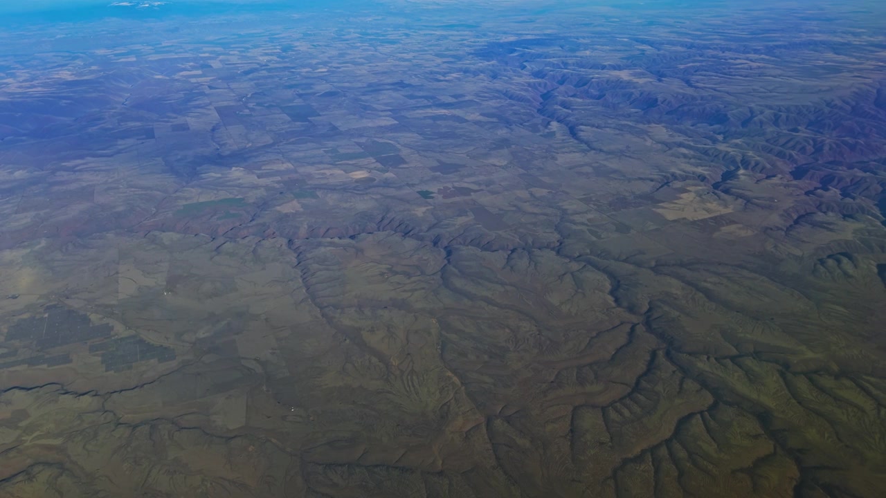 Aerial of rolling mountain terrain and deep valleys from passenger aircraft, aerial