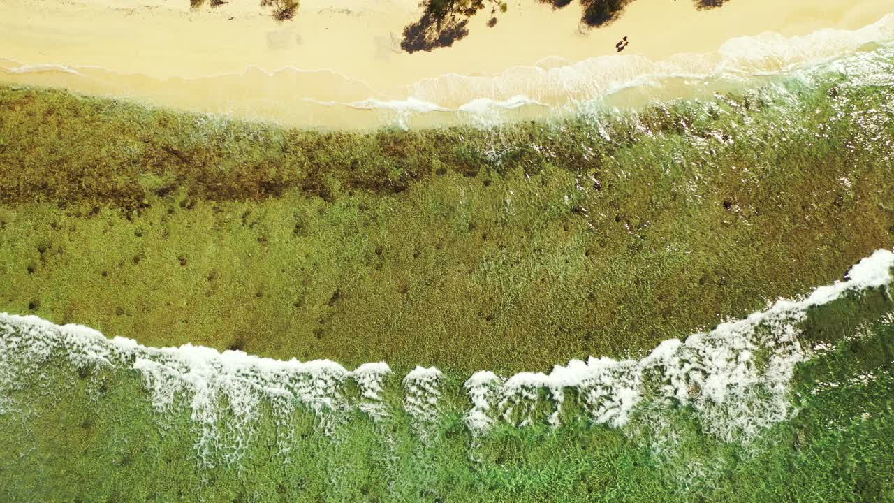 A couple walking along the tropical beach in Thailand. Waves rolling on the sandy shore