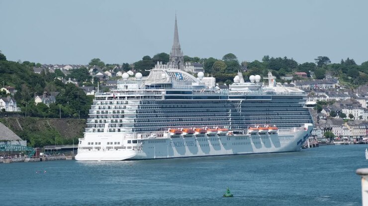 Large cruise ship docked at Cobh promenade in Ireland, with cathedral tower being the only thing standing taller then ship