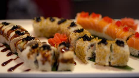 the close up video of freshly made 3 different types of uramaki sushi on the plate with ginger under soy sauce