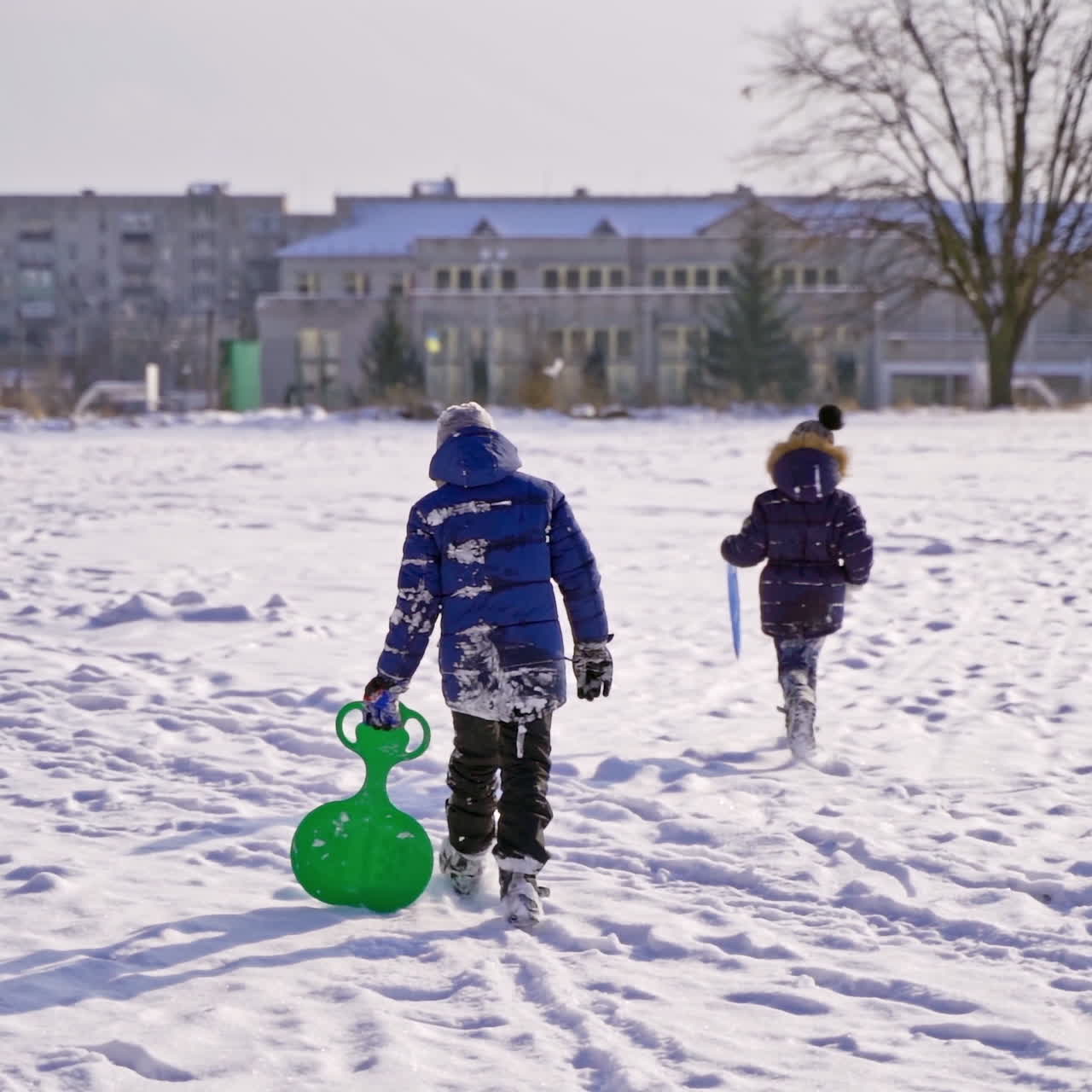 Frost winter season. Two children walk a winter road with plastic spade sledges. Winter games and fun. Kids having winter vacation. Slow motion.