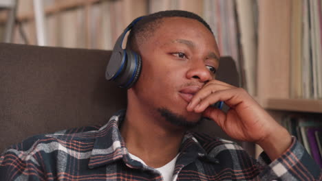 upset man listens to music via earphones in library closeup. black guy with wireless headphones rests sitting by bookcase. audiobook listening