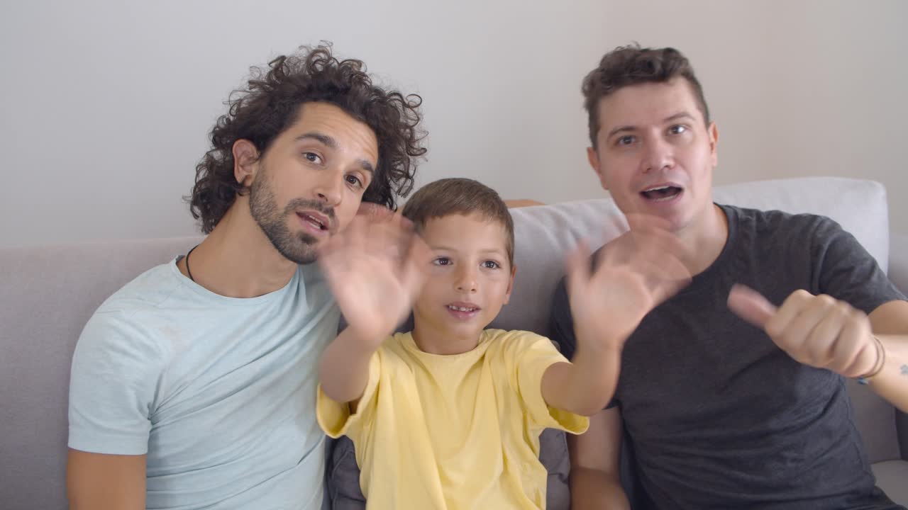 Due papà felici e un bambino che salutano la telecamera