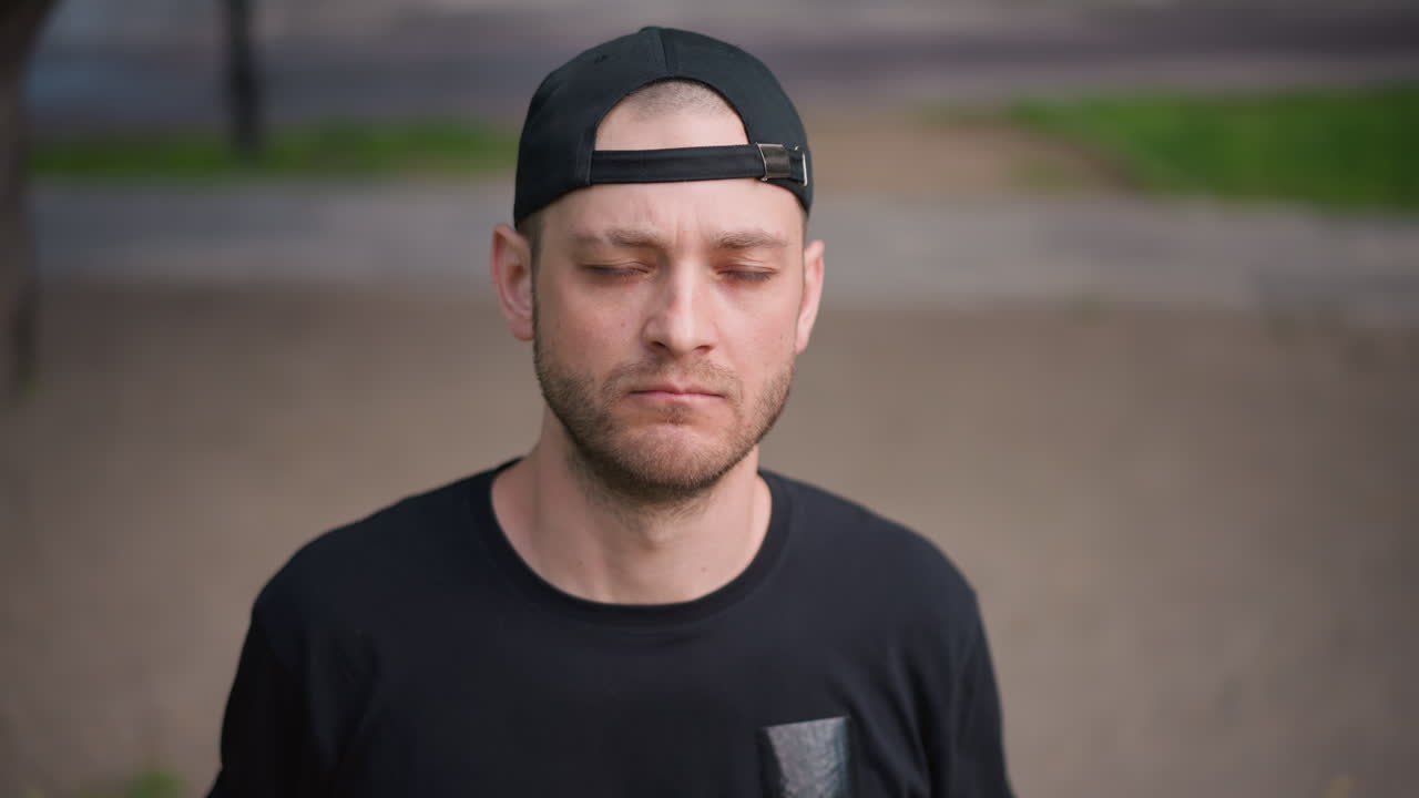 white man contemplative in park, cap turned backward, eyes closed between sets. Former boxer reviewing strategy, street artist pausing for breath, coach reflecting on workout intensity, soft daylight