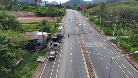 aerial tracking shot of person on scooter driving on street in thailand - holiday trip in asia - following flight