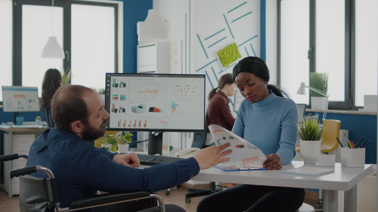 Black manager woman talking with paralysed team leader checking graphs