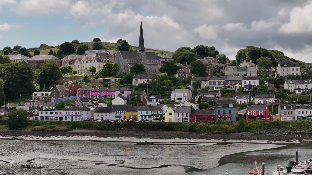 Et autentisk luftfoto af den farverige kystby Crosshaven i Irland, med traditionel arkitektur og et fremtrædende kirketårn med udsigt over havnen.