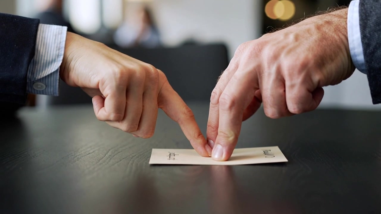 Mani di professionisti che premono gli indici su una busta a un tavolo da riunione, a significare un accordo, con i polsini in vista.
