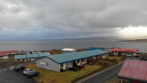 Drone-Flying-over-Multi-Colored-Coastal-Houses-over-the-Ocean-Revealing-Awe-Inspiring-Sunset-over-Mountains,-Reykjavík-Iceland