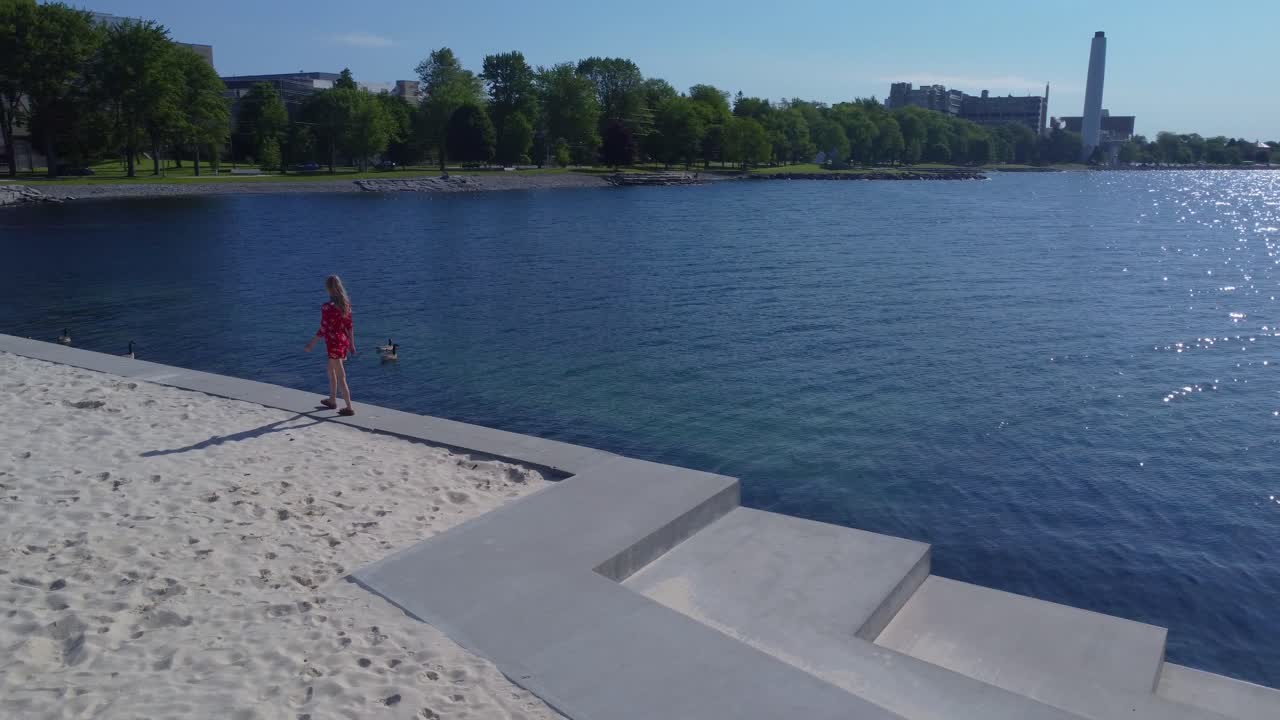 귀여운 빨간 드레스를 입고 해안가를 따라 걷는 젊은 여성의 추적 샷