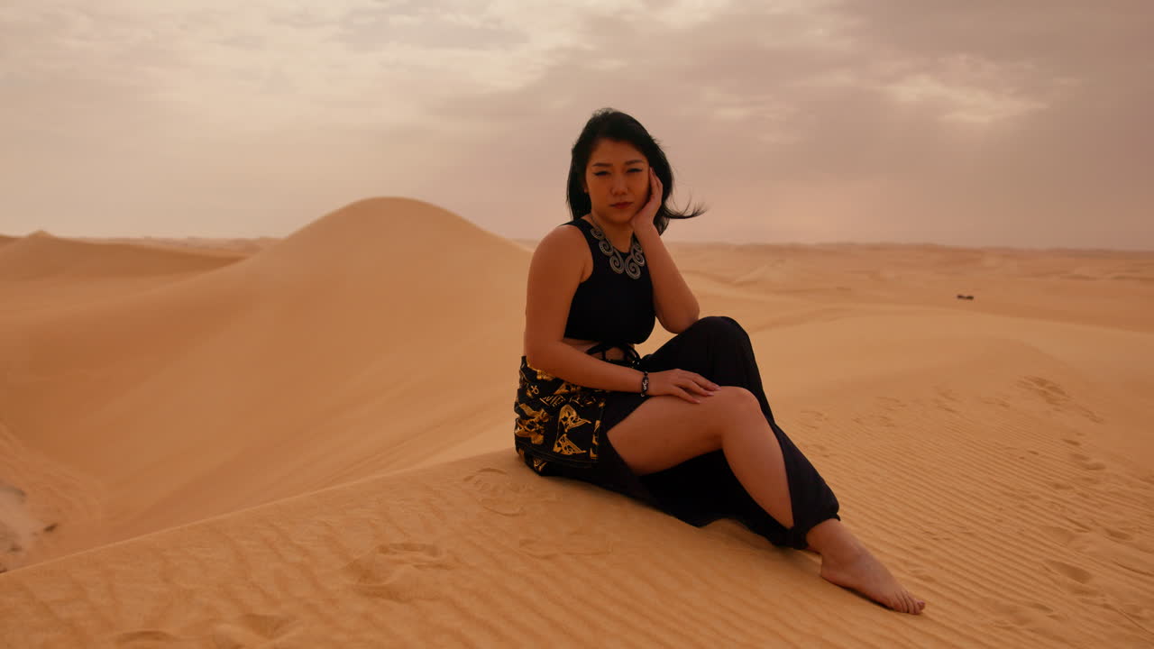 hermosa modelo asiática sentada en una duna de arena en el desierto del sáhara