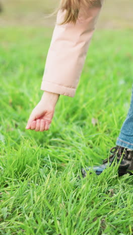 primer plano de la pierna de una joven en vaqueros azules y zapatos negros jugando en la hierba verde exuberante. ella juega usando su mano para tocar la hierba, capturando un momento de alegría despreocupada y actividad al aire libre