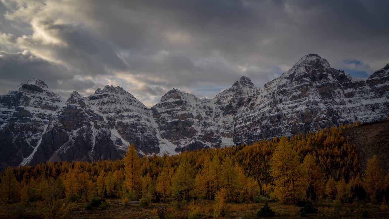 Timelapse, nuvole scure e drammatiche si muovono sopra cime innevate e una valle di larici in una fredda giornata autunnale nel Parco Nazionale di Banff, Canada.