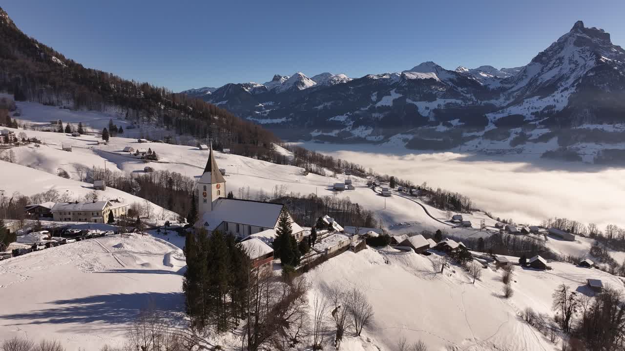Drone flight over the snow-covered village of Amden with mist shrouding Lake Walensee in the background.