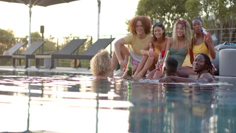 Happy-diverse-friends-with-drinks-talking-at-pool-and-swimming-in-slow-motion