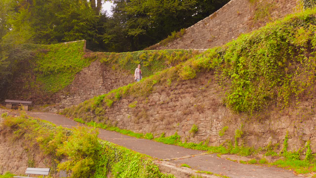 A woman climbs the stone-walled rampes du Loch, from the historic Saint-Goustan port up to the town of Auray. Features ancient stone, ivy, and lush vegetation
