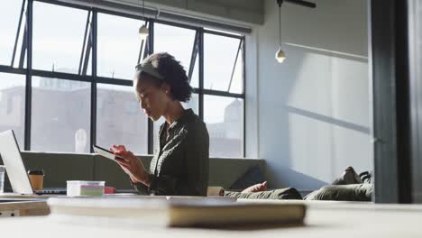 african american businesswoman sitting at table and using smartphone at office