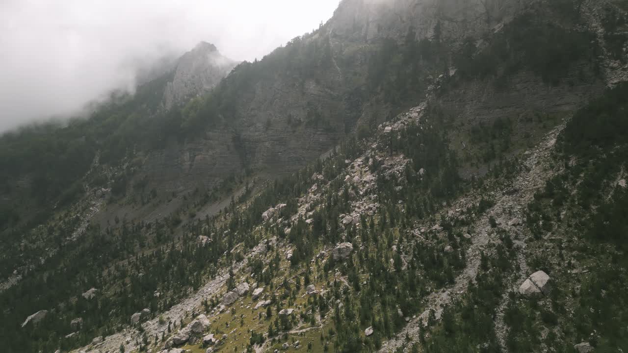 Misty mountain valley with scattered rocks and green trees along the Valbona Pass in Albania