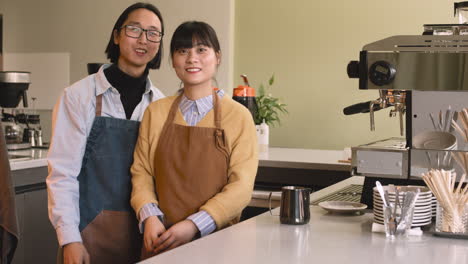 two waiters smiling at camera while standing behind counter in a coffee shop