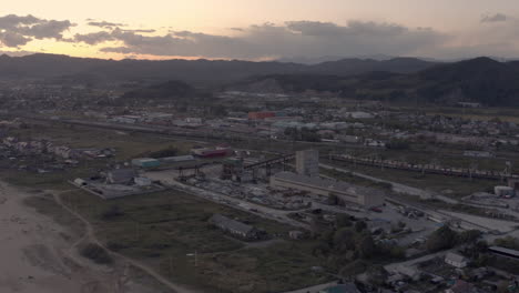 Concrete-making-factory-industrial-complex-near-seaside-in-the-evening-with-town-buildings-in-the-background,-Far-East,-Russia