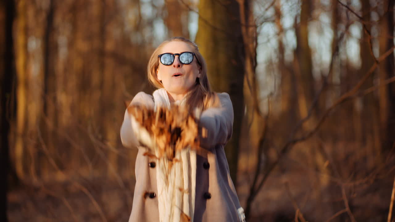 позитивная счастливая женщина бросает листья осенью в парке