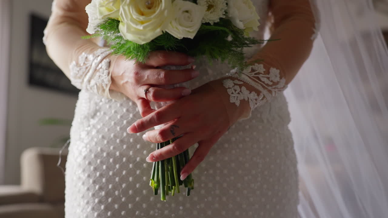 Primo piano delle mani di una sposa caucasica con un abito da sposa bianco che tiene fiori di rosa