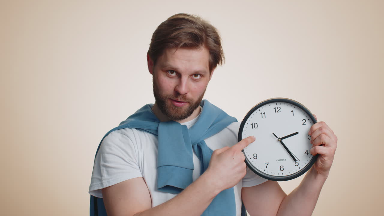 Smiling man showing time on wall office clock ok thumb up approve pointing finger at camera