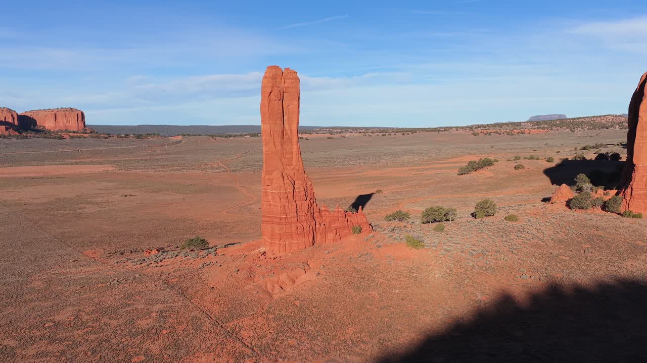 A cinematic drone rotation circles an epic red rock spire monolith, emphasizing the mystical verticality and rugged sandstone beauty of a legendary landmark within a remote desert vista