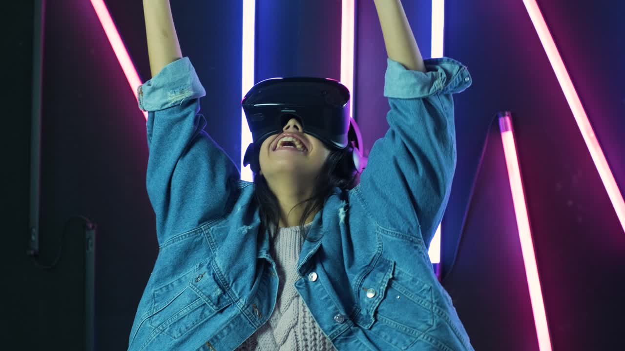 una giovane donna felice si guarda intorno e si chiede quanto sia sorprendente l'auricolare vr. casco di realtà virtuale sullo sfondo di illuminazione a colori
