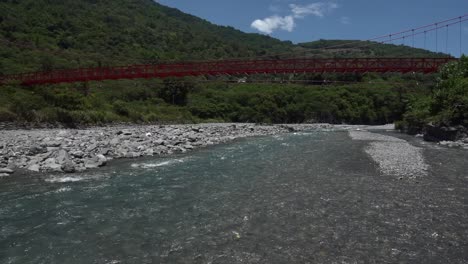 river flowing under red suspension bridge on tropical island