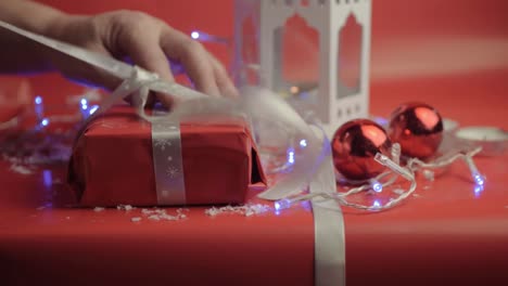 unwrapping christmas gift with ribbon and red paper with red background and baubles