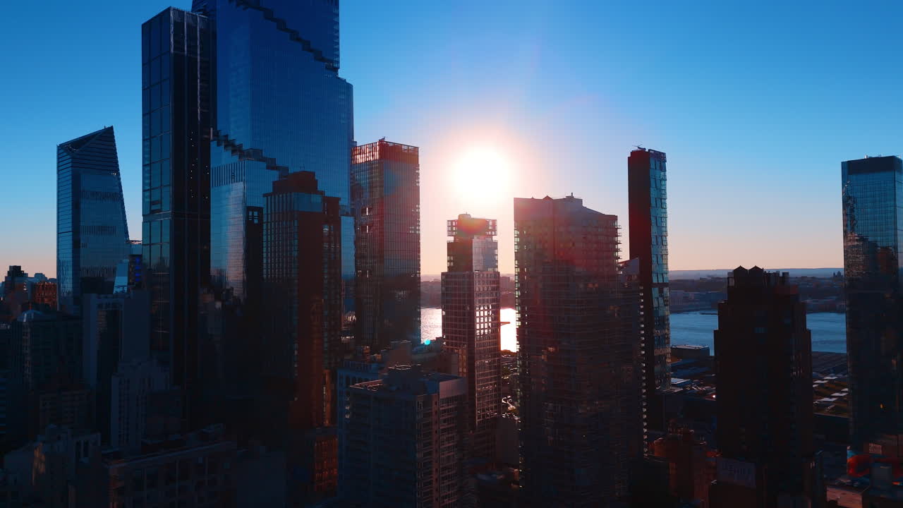 Arranha-céus de Manhattan e o Rio Hudson ao pôr do sol. Edifícios modernos em silhueta contra o sol brilhante e o rio, em Nova Iorque, durante a hora dourada.