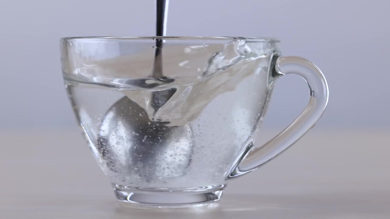 Cucchiaio di metallo che mescola liquido trasparente in un bicchiere di vetro