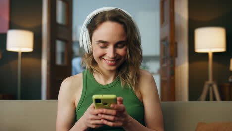 relaxed lady listening headset music at sofa. smiling girl turning smartphone