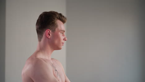 determined shirtless fighter with chest tattoo pulls resistance rope during home hallway workout, maintaining intense gaze through window while building upper body strength