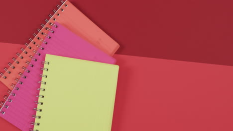 überblick über farbenfrohe notizbücher mit kopierplatz auf rotem hintergrund, in zeitlupe